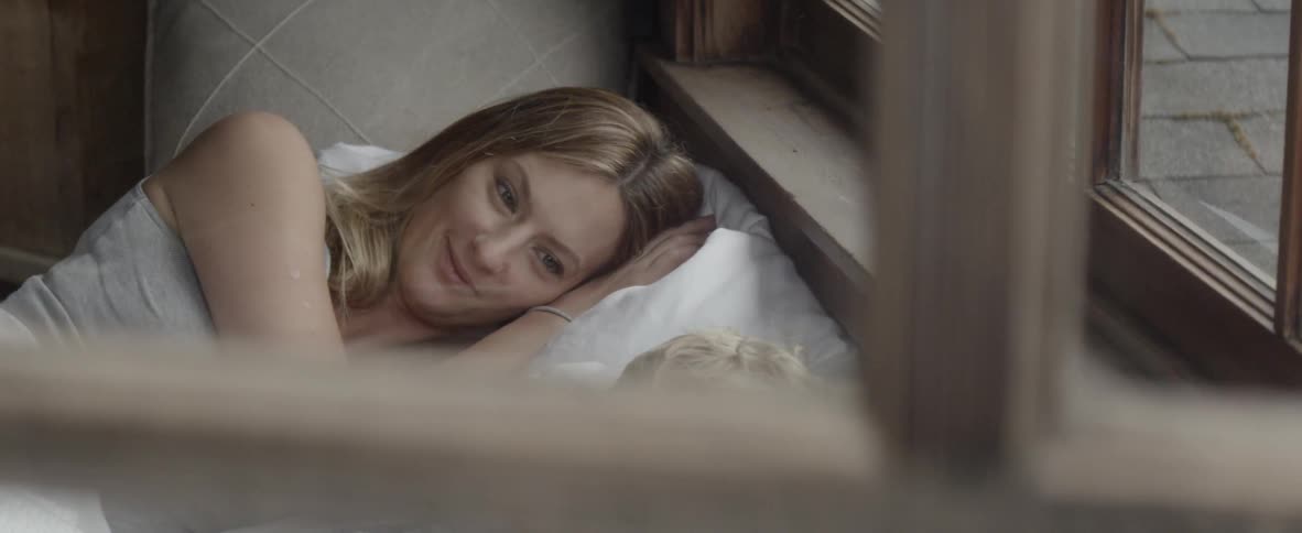 A woman smiles as she talks to her son while they lay in bed