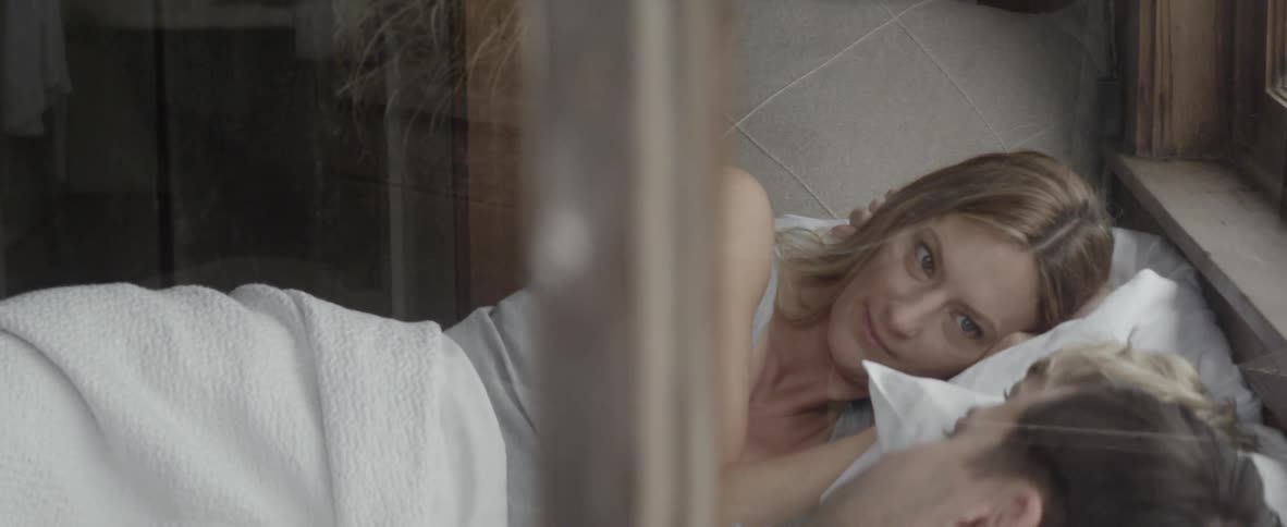 A woman lays on the bed and talks to a man