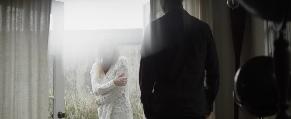 Man watches a woman in a white sweater hug herself