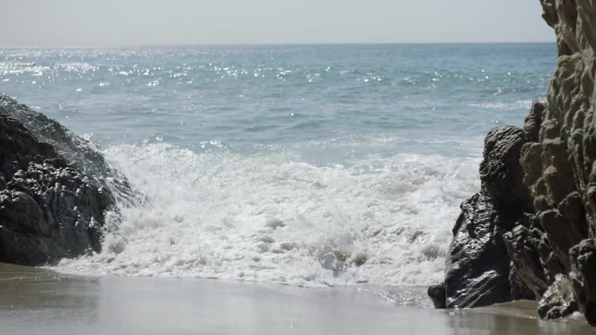 Waves crash against some rocks by the beach