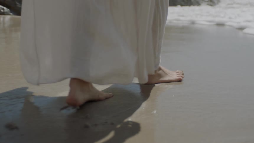 A woman with a long white dress walks into ocean waves