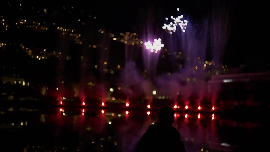 Fireworks are going over over water as someone watches