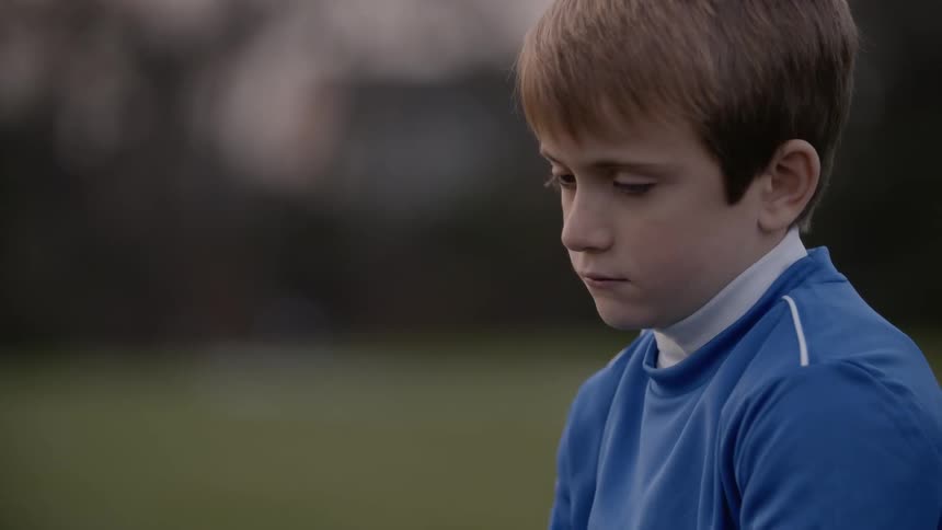 A boy looks sad outside at sunset