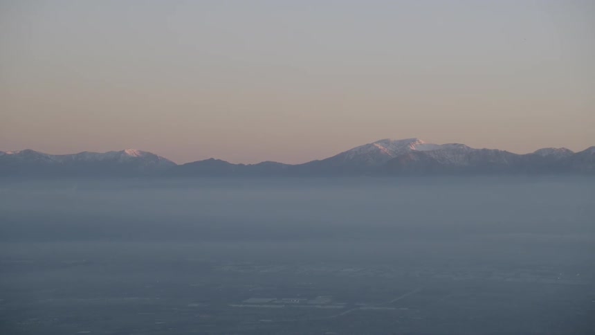 Distant snow capped mountains rise above the mist at sunrise