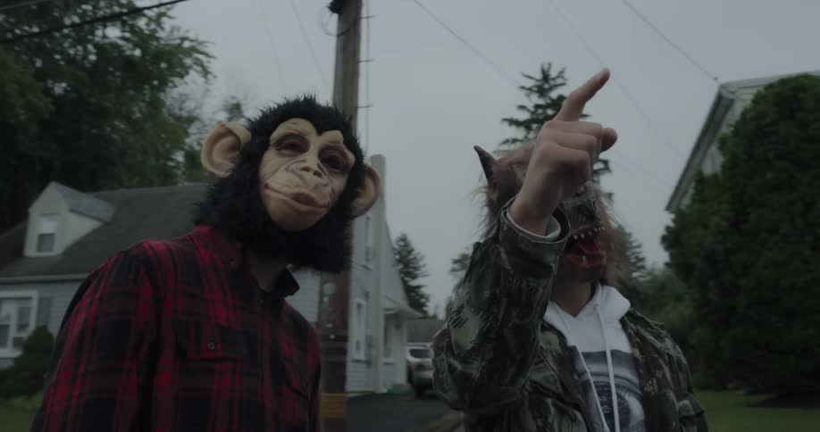 A couple of people are wearing animal masks and pointing at something on a neighborhood street