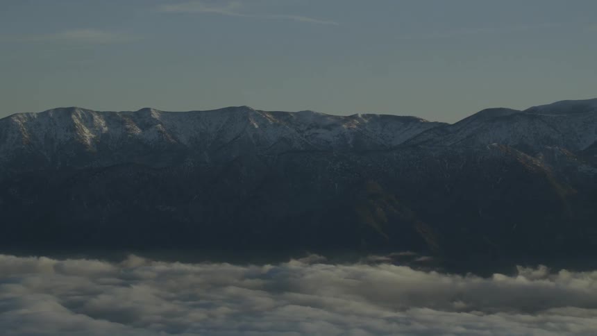 Clouds float near a snowy mountains