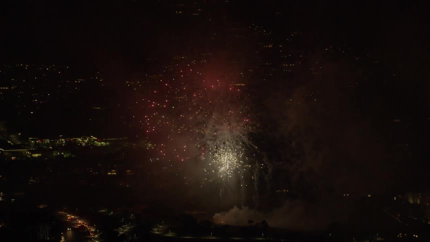 Fireworks burst in the sky over a city while cars travel on the highway