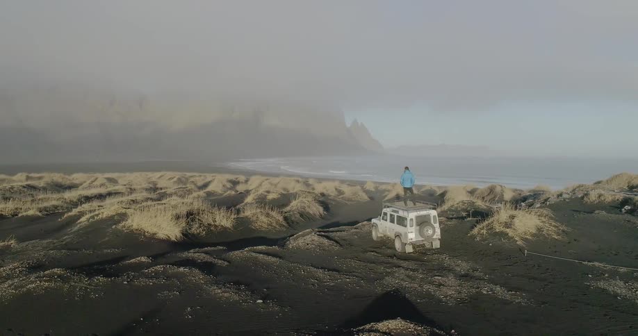 A person stands on top of a vehicle while parked on a beach
