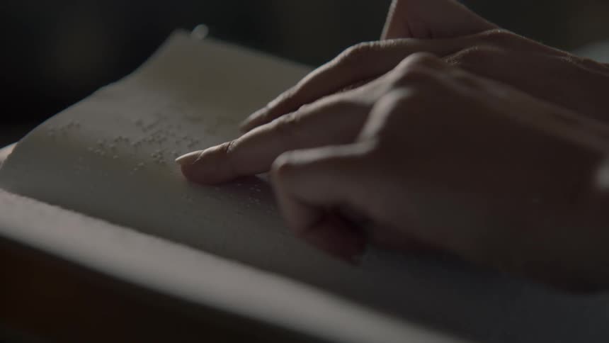 A woman's hands are shown as she reads braille from a book