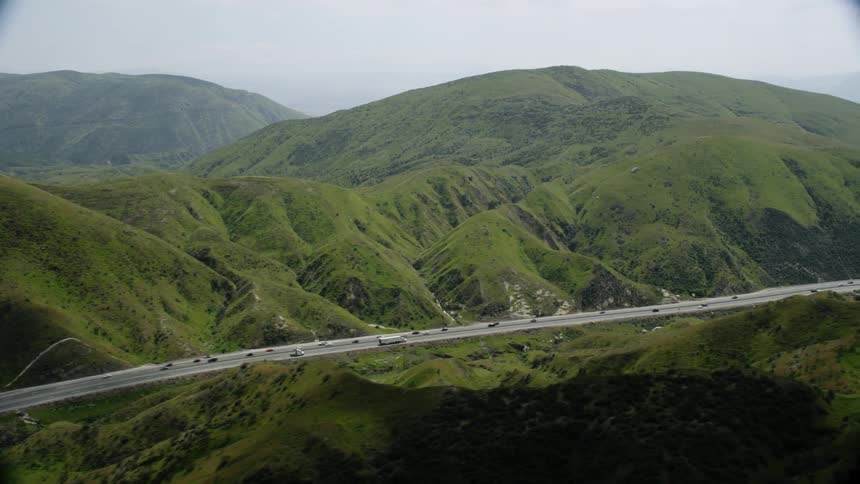Vehicles travel on a highway between the green hills