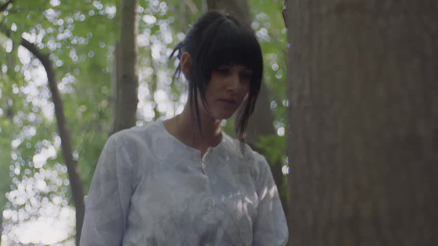 A woman stands near tall trees