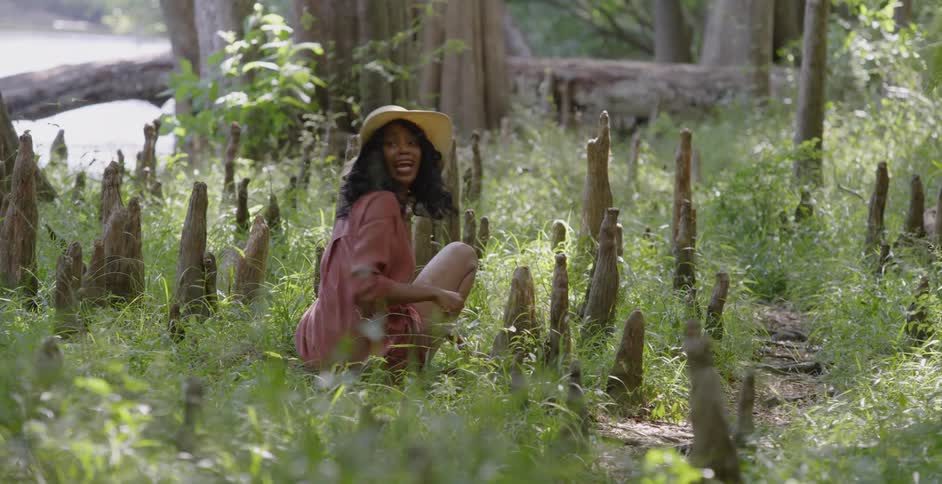 A woman sitting in the grass waves someone over