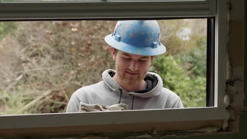 A construction worker is smiling and talking as he works outside in daylight