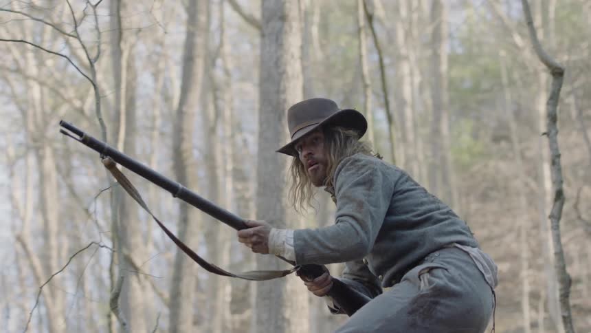 A soldier searches and aims in a forest with a rifle