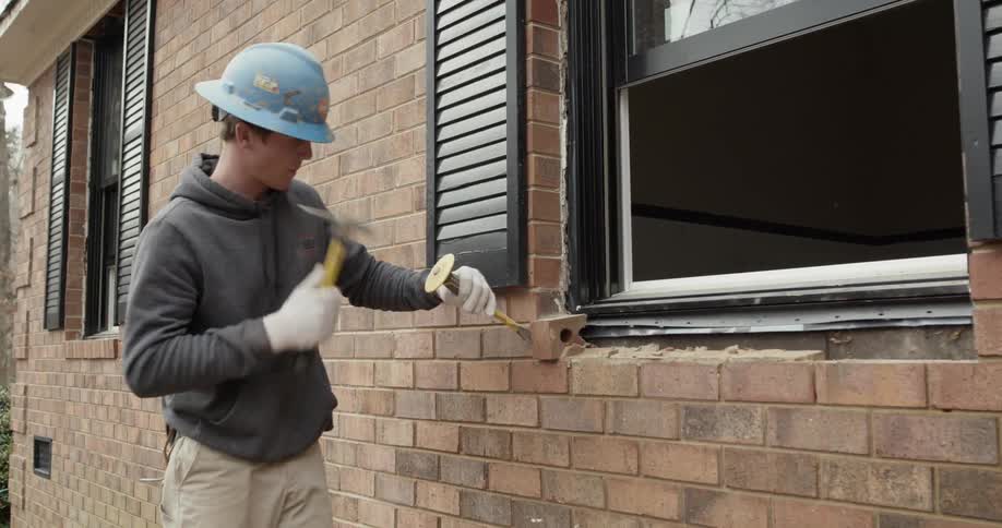 A construction worker removes brick from a window ledge