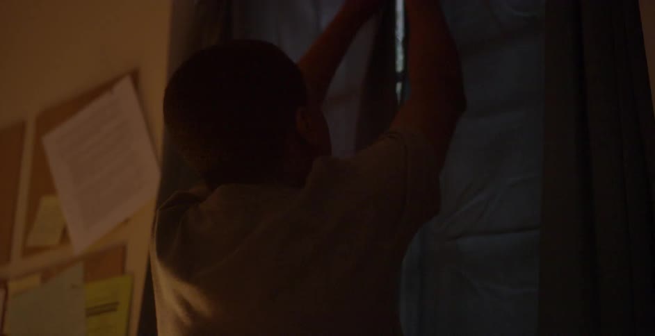 A young boy closes curtains on a window as it rains outside