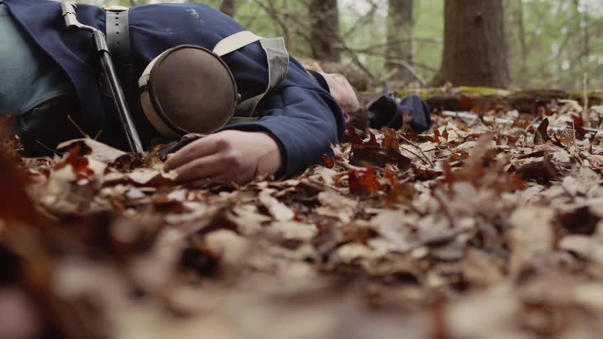 Feet walk past a soldier lying on the ground