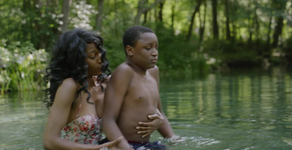 A woman helps a scared boy swim in a lake