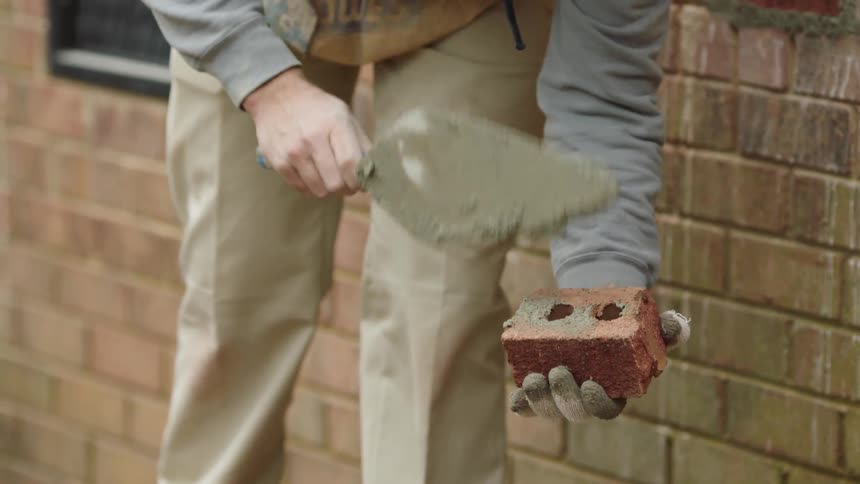 A man muds a brick with a trowel