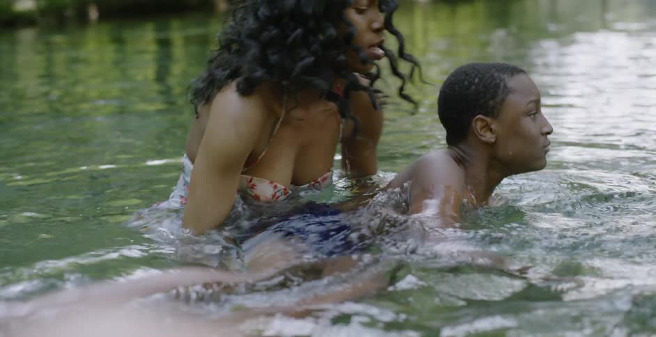 A woman helps a fearful young boy swim in a river