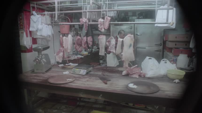 A man is working in a butcher shop in an outdoor market in asia at night