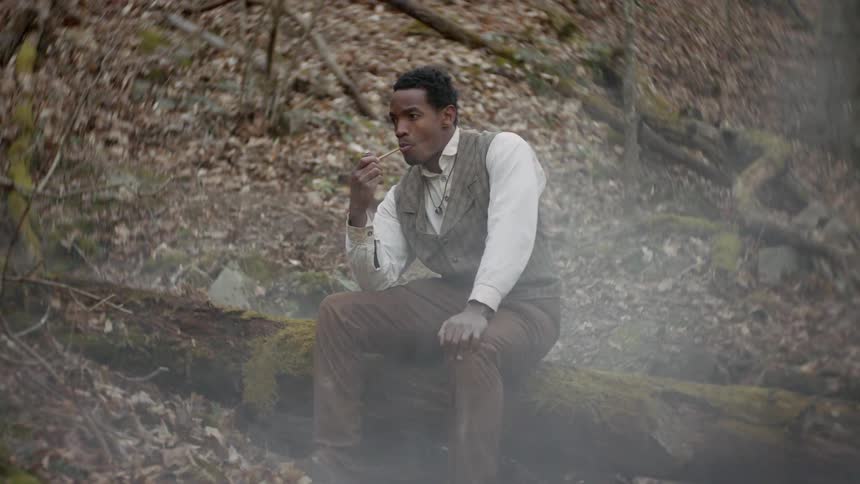 A man smokes a pipe on a tree log