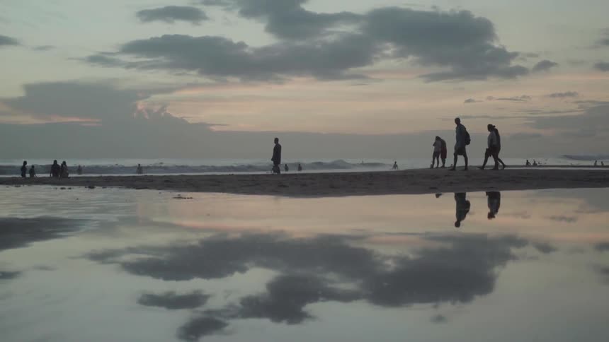 Several people walk on the beach at sunset