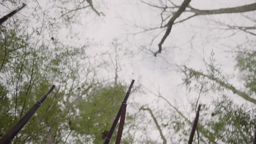 Two soldiers aim their guns and shoot in the woods at the same time