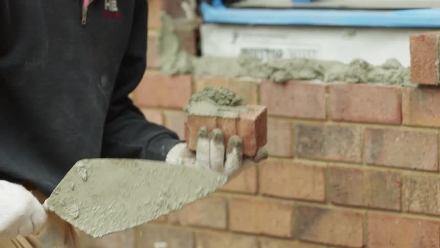 A construction worker lays brick on a windowsill