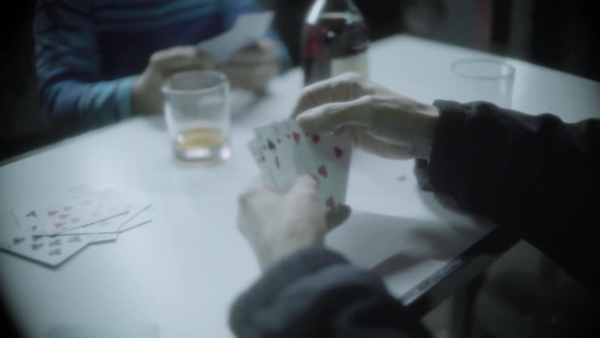 People sit at a table drinking whiskey and playing cards