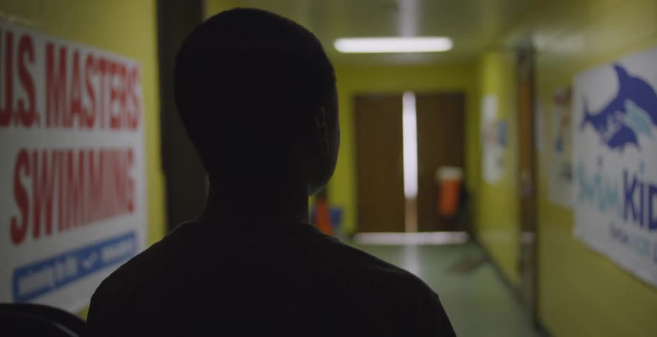 A young man walks down a dim hallway