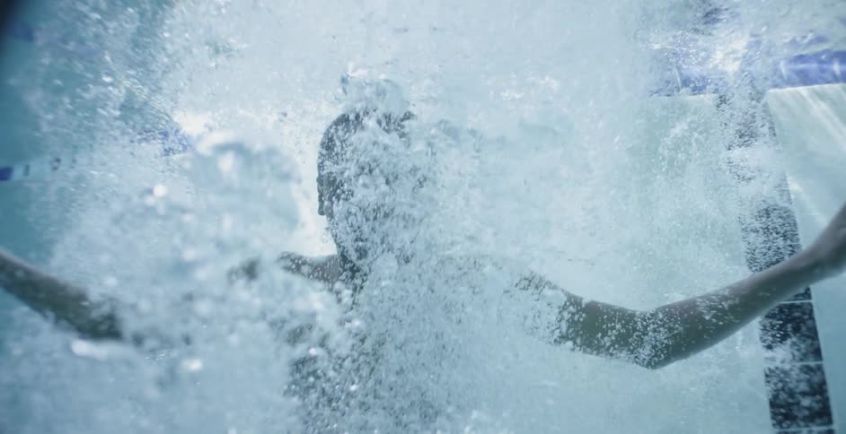 A boy jumps into a swimming pool and is floating underwater in daylight