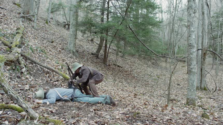 A man fires a rifle while standing over a fallen soldier