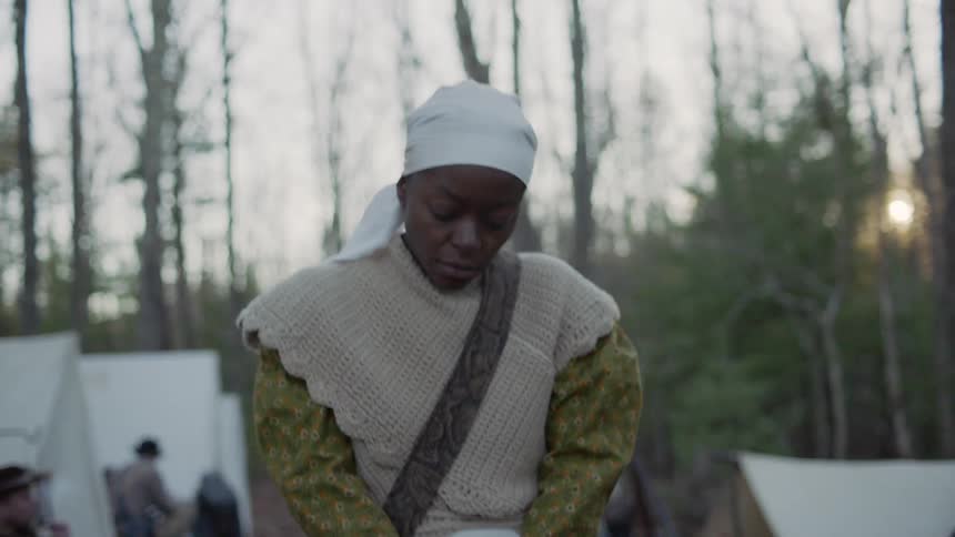 A slave woman is walking through a confederate camp at sunset