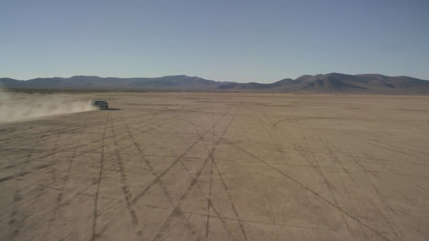 A vast moving vehicle on a large barren field towards some mountains