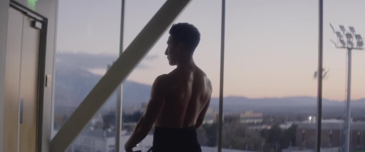 A man prances in a room with tall glass windows