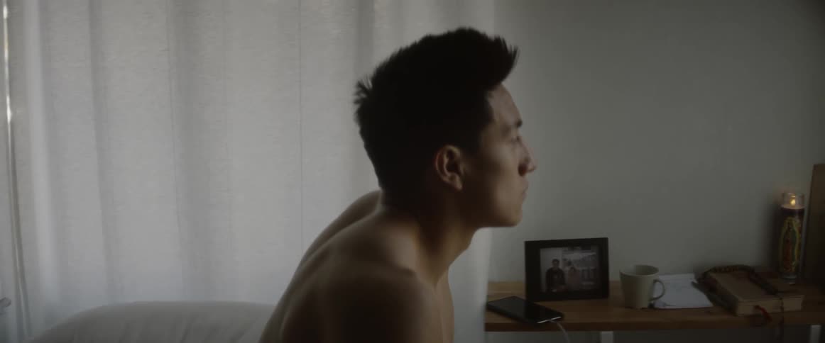 A shirtless man sits in bed