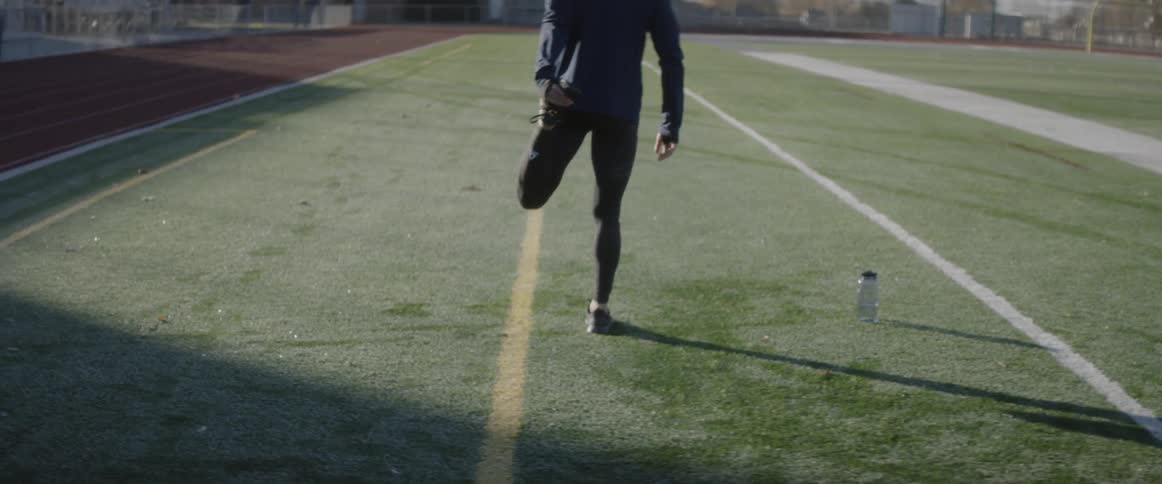 A man is stretching his legs as he prepares to run down a track in daylight