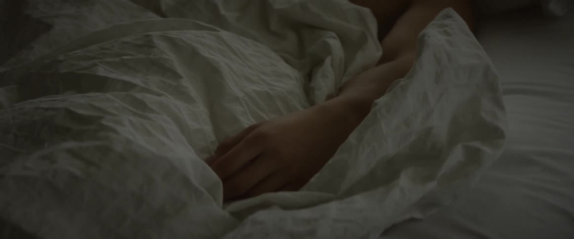 Person lays in bed with their hand resting on the sheet