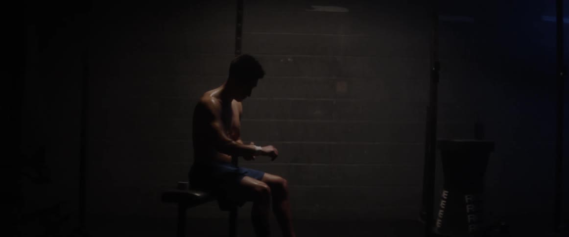 A shirtless man wraps his wrist with athletic tape