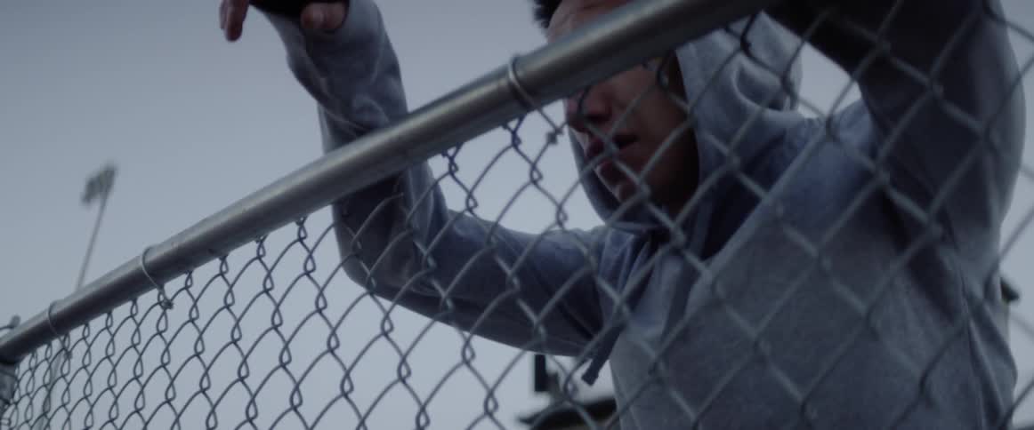 Man leans against chain link fence crying