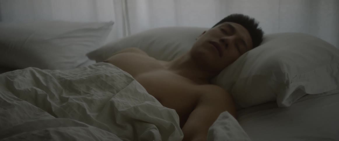 A shirtless man sleeps in bed
