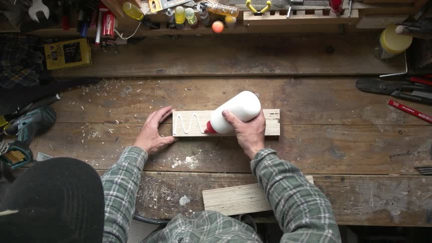 A man glues two objects together on a workbench
