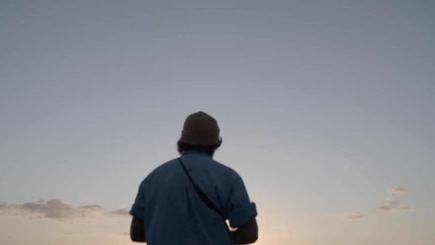 Person in hat looks out over the water at sunset