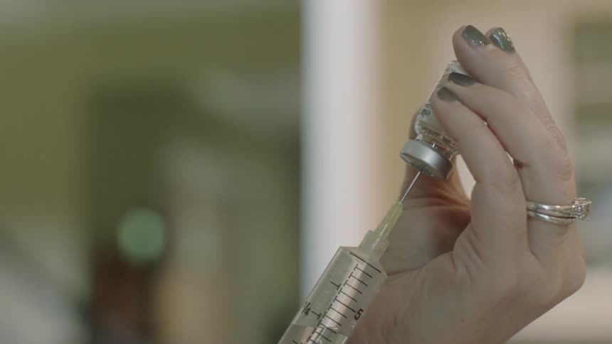 A person fills a needle from a vial