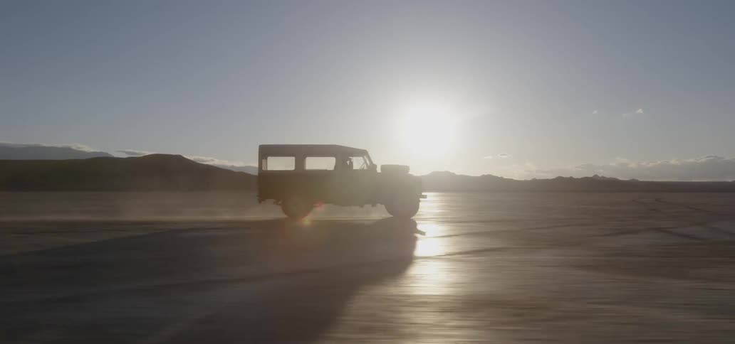 Vehicle drives across rural field at sunset