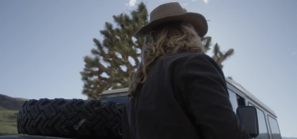 A man with a cowboy hat stands outside on a windy day