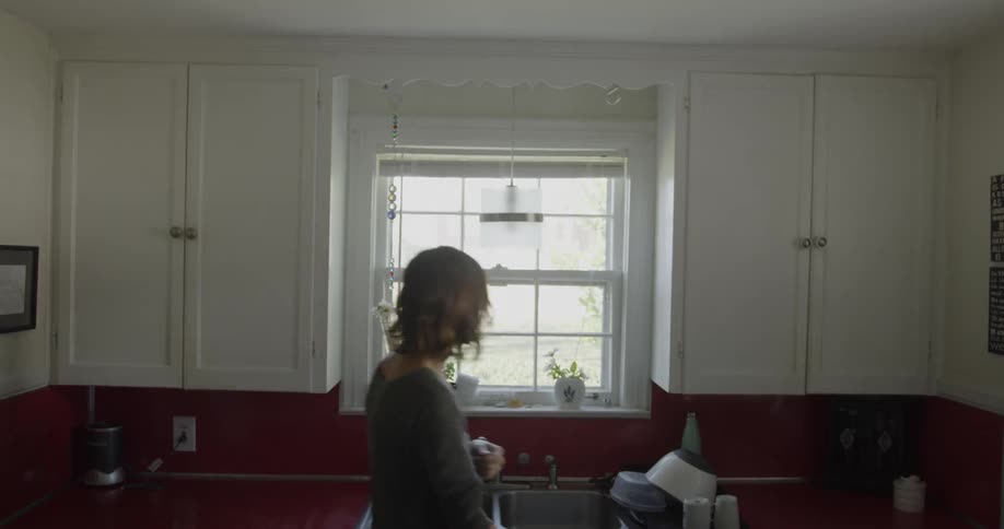 A woman is putting away dishes and using the sink