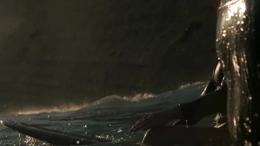 A surfer swims in the ocean at sunset