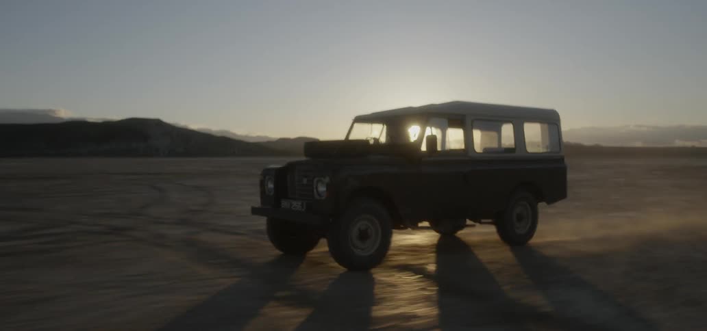 A vehicle drives across a dirt field at sunset